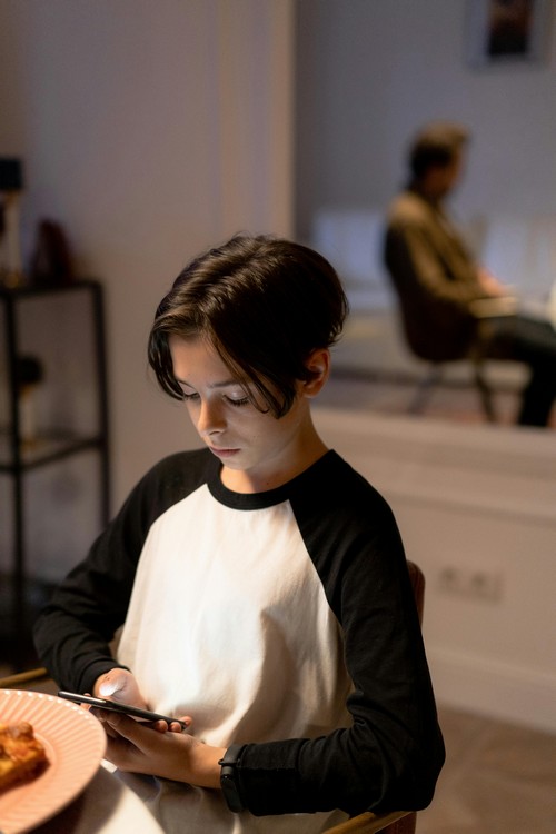 Teenage boy sitting at restaurant table looking at his phone screen