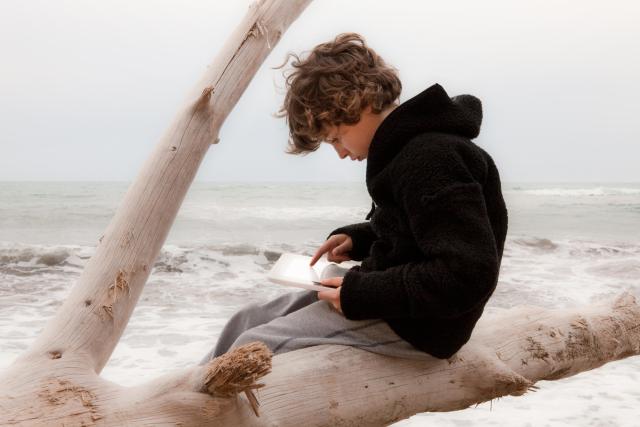 Young boy sitting on a log with the sea in the background