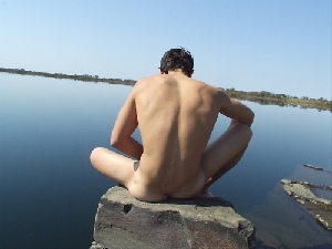 View from the back of a nude man sitting on a rock